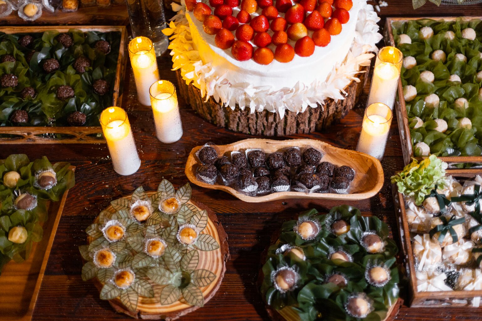 Mesa de doces rústica com bolo de morangos, brigadeiros e velas acesas