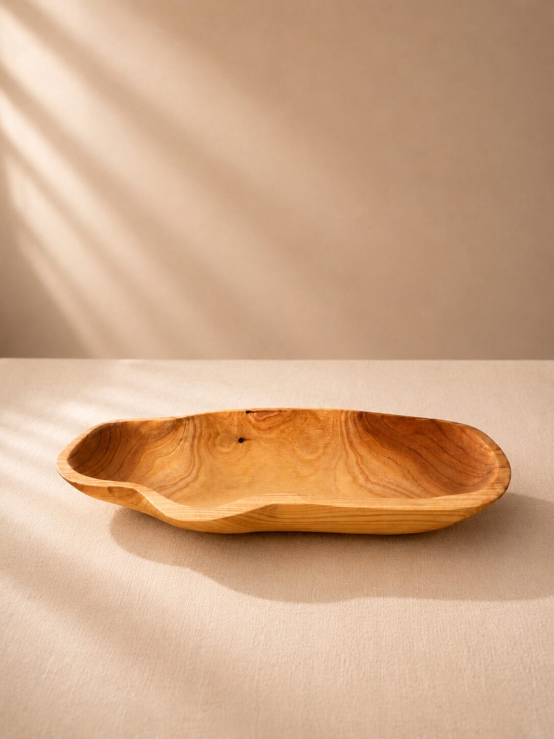 Travessa oval de madeira esculpida em formato orgânico sobre mesa bege